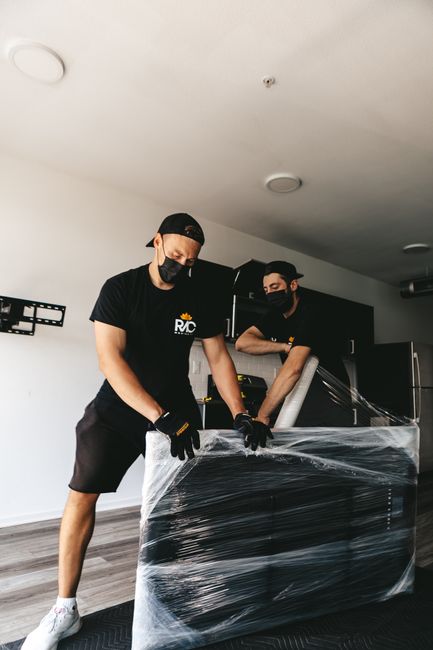 Two professional movers from Man with Van Lower Morden are inside a modern, well-lit residential property, carefully preparing to transport a large, heavy appliance or piece of furniture. Both movers 